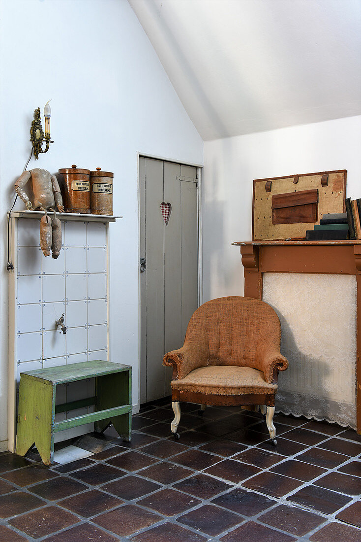 Old armchair and flea-market finds on dark terracotta tiled floor