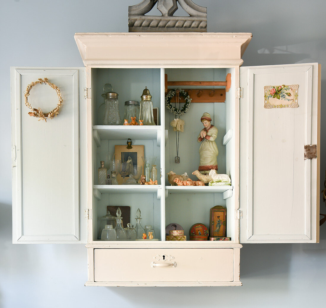 Collection of little, old bottles and vintage-style ornaments in wall-mounted cabinet