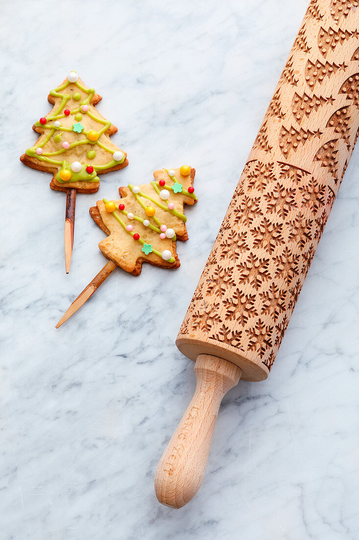 Rolling pin with Christmas motifs and Christmas tree biscuits on a stick
