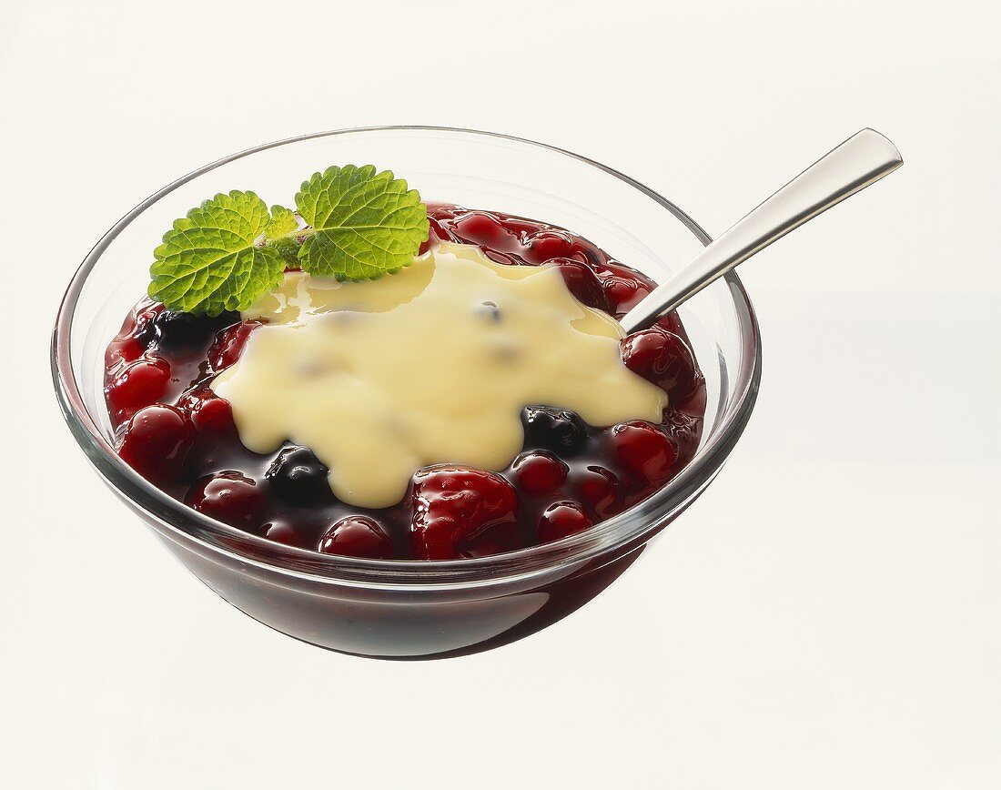Red fruit compote with custard in glass bowl with spoon