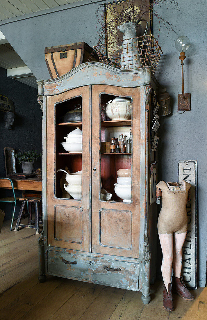 Mannequin next to old glass-fronted cabinet containing soup tureens