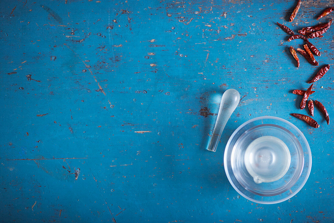 Glass mortar, pestle and dried chili on blue wooden surface