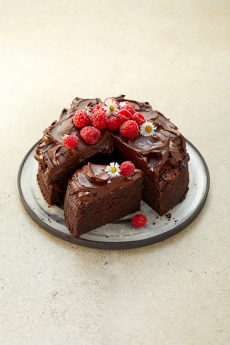Laktosefreier Schokoladenkuchen dekoriert mit Himbeeren und Gänseblümchen