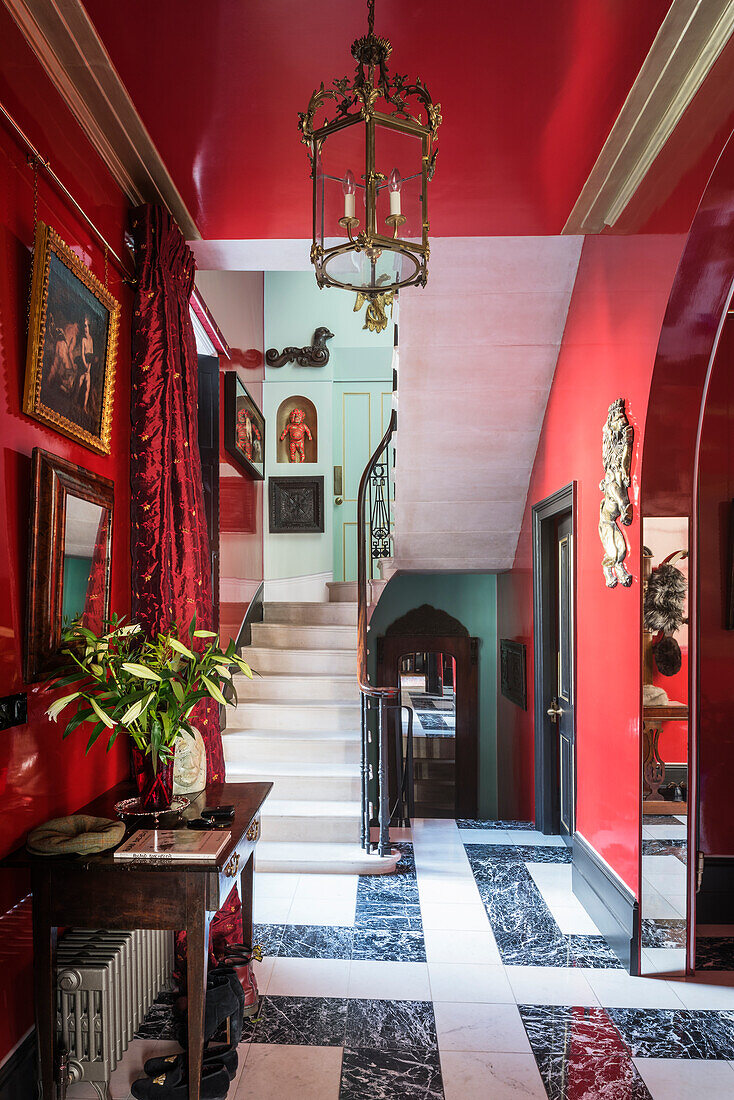 Mahogany table in hallway with red walls, black-and-white marble floor, mirror and paintings on the wall