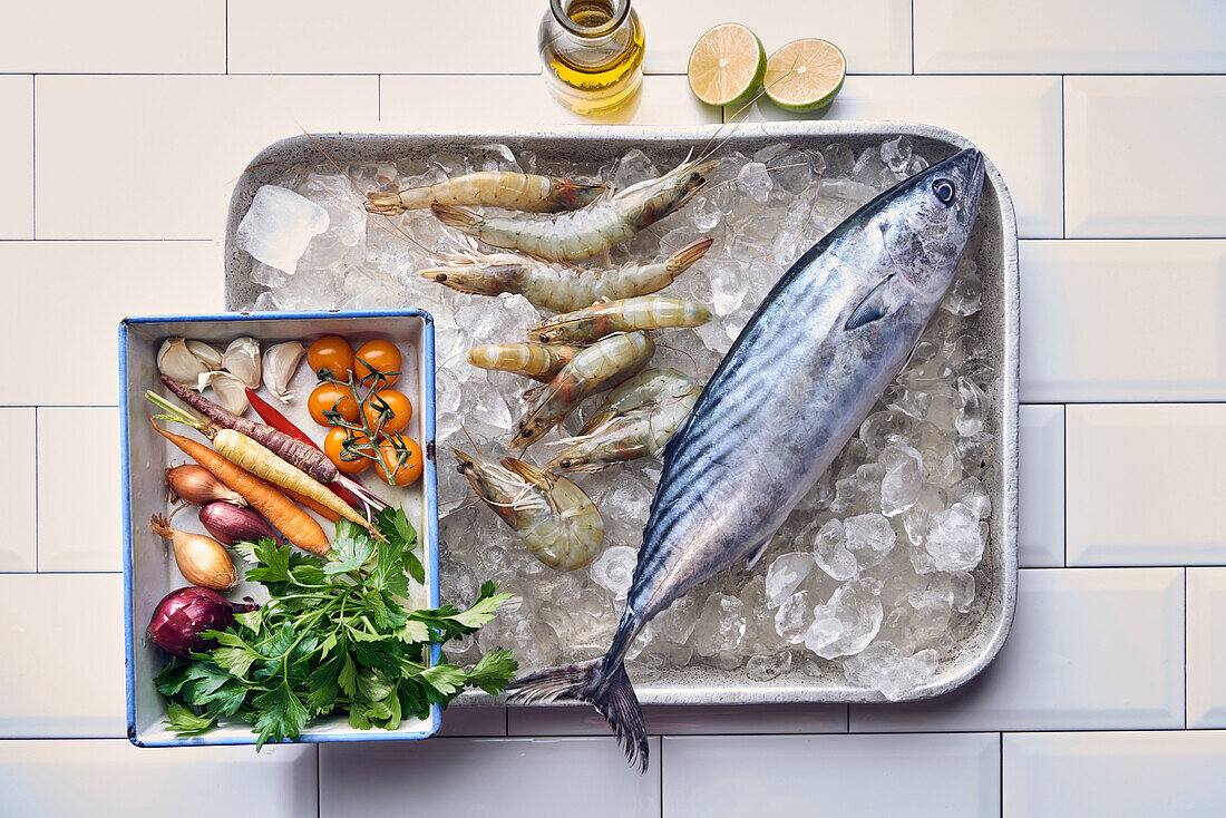 Bonito and tiger prawns on ice next to fresh vegetables and herbs