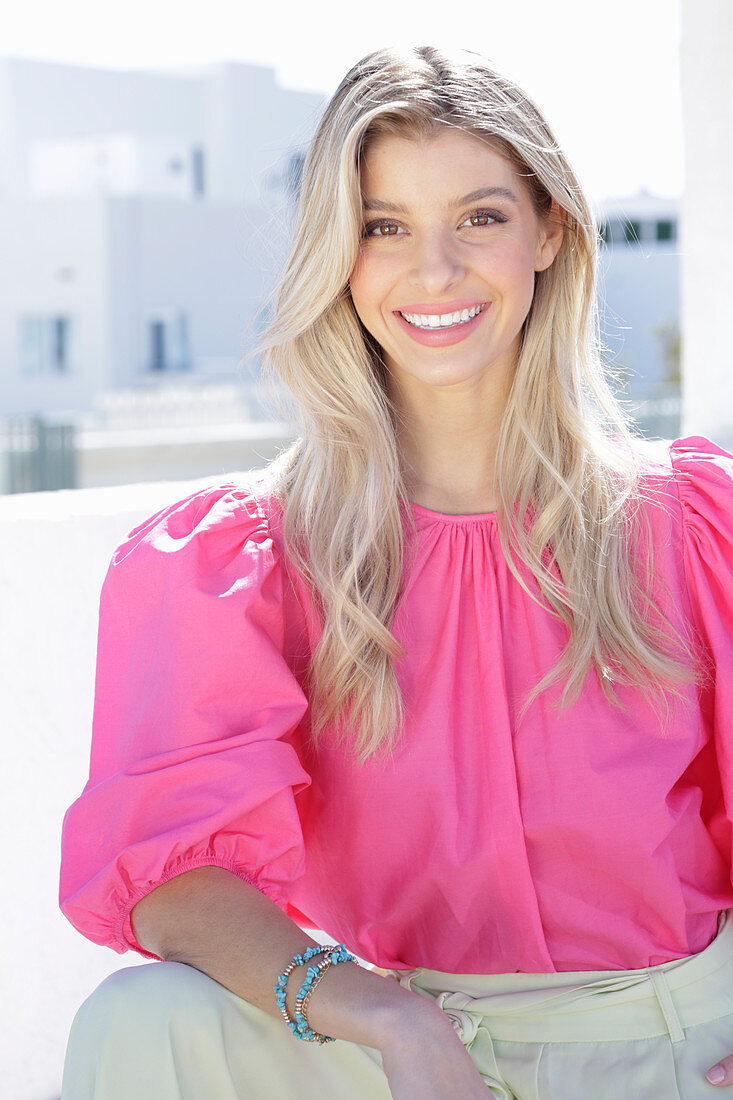 Junge blonde Frau in pink Bluse mit Puffärmel und weißer Sommerhose