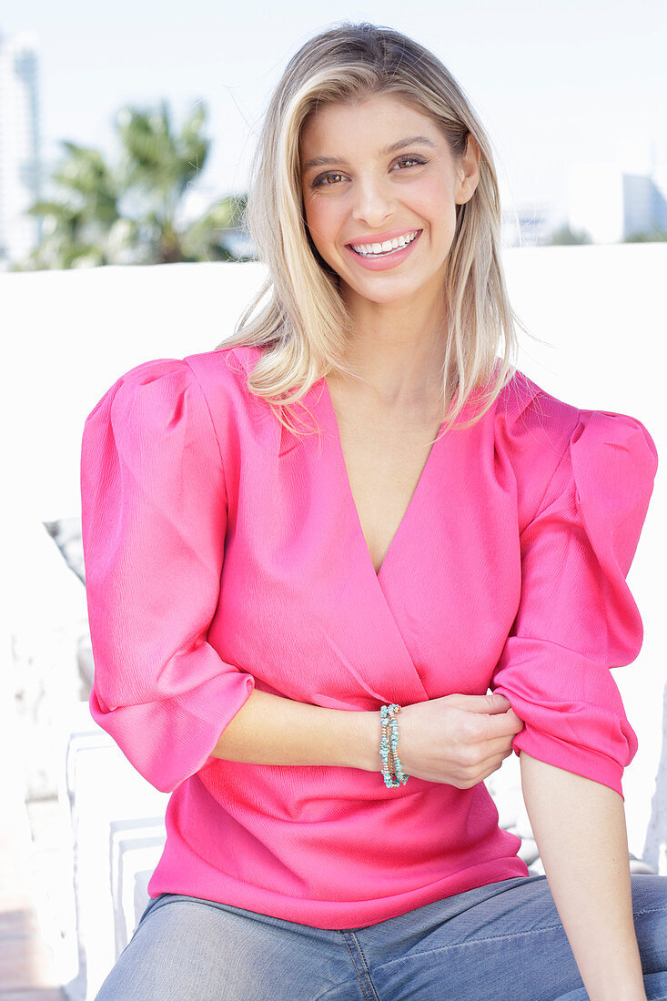 A young blonde woman wearing jeans and a pink wrap-around top with puffed sleeves