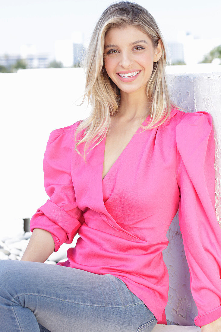 A young blonde woman wearing jeans and a pink wrap-around top with puffed sleeves