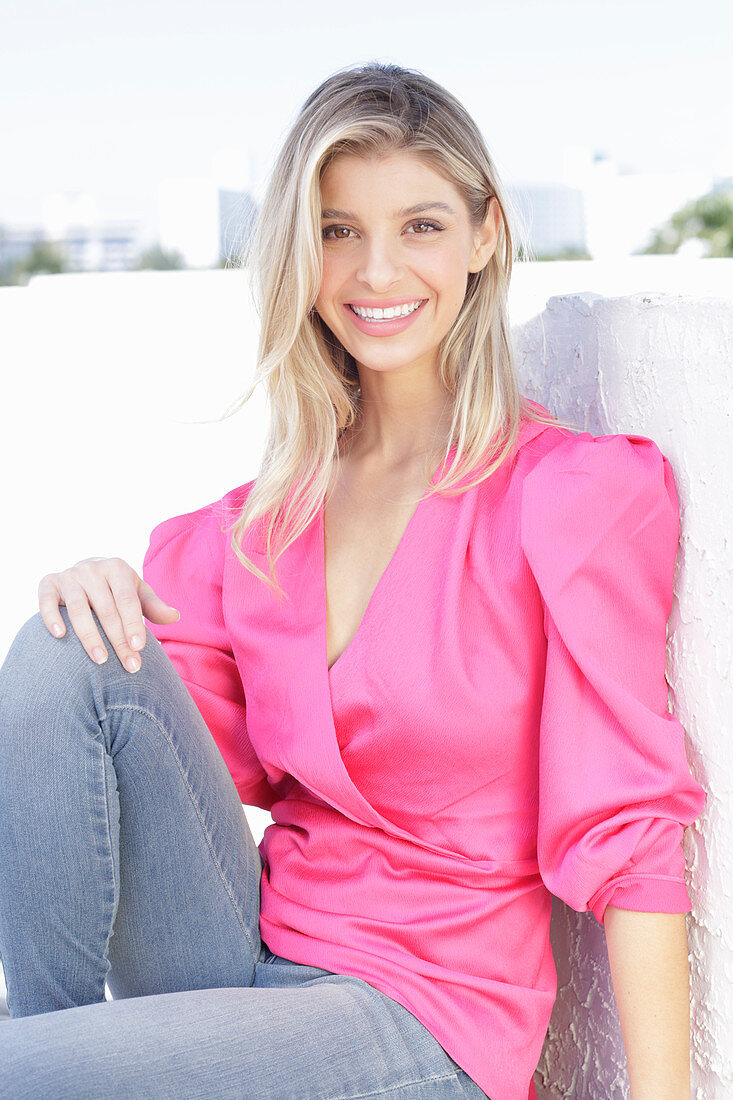 A young blonde woman wearing jeans and a pink wrap-around top with puffed sleeves
