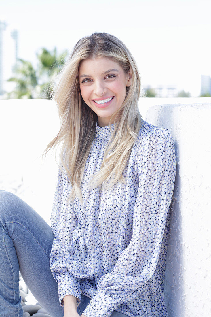 A young blonde woman wearing a blue-and-white patterned top and jeans