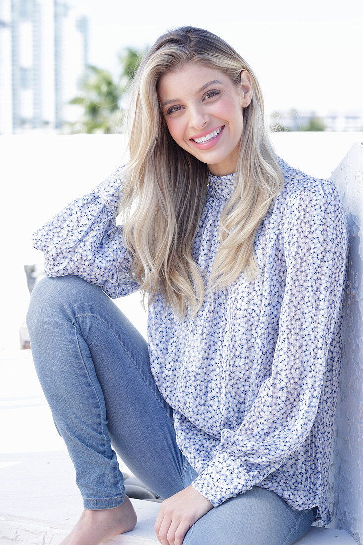 A young blonde woman wearing a blue-and-white patterned top and jeans