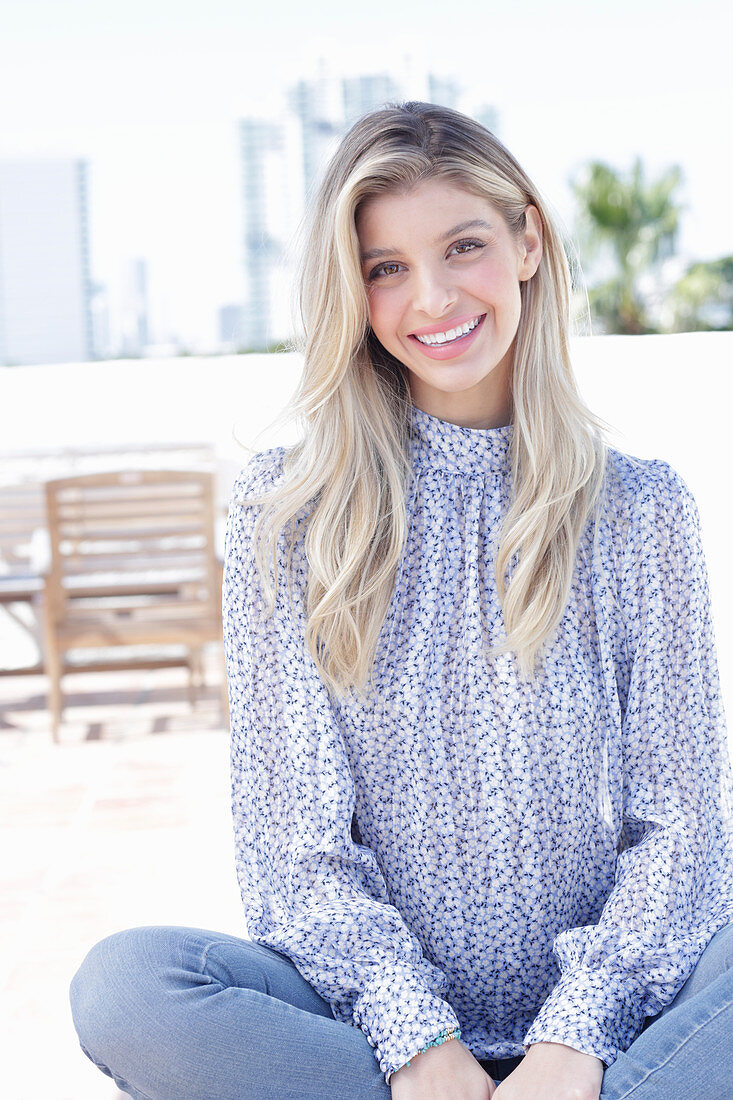 A young blonde woman wearing a blue-and-white patterned top and jeans