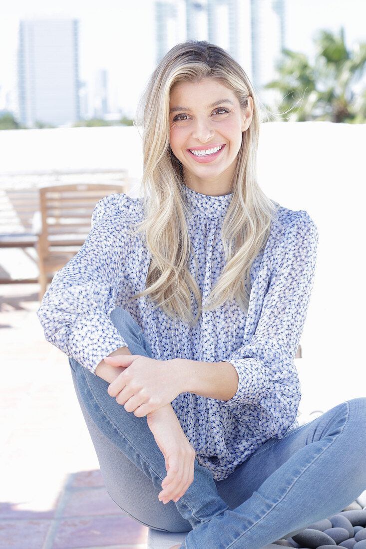 A young blonde woman wearing a blue-and-white patterned top and jeans