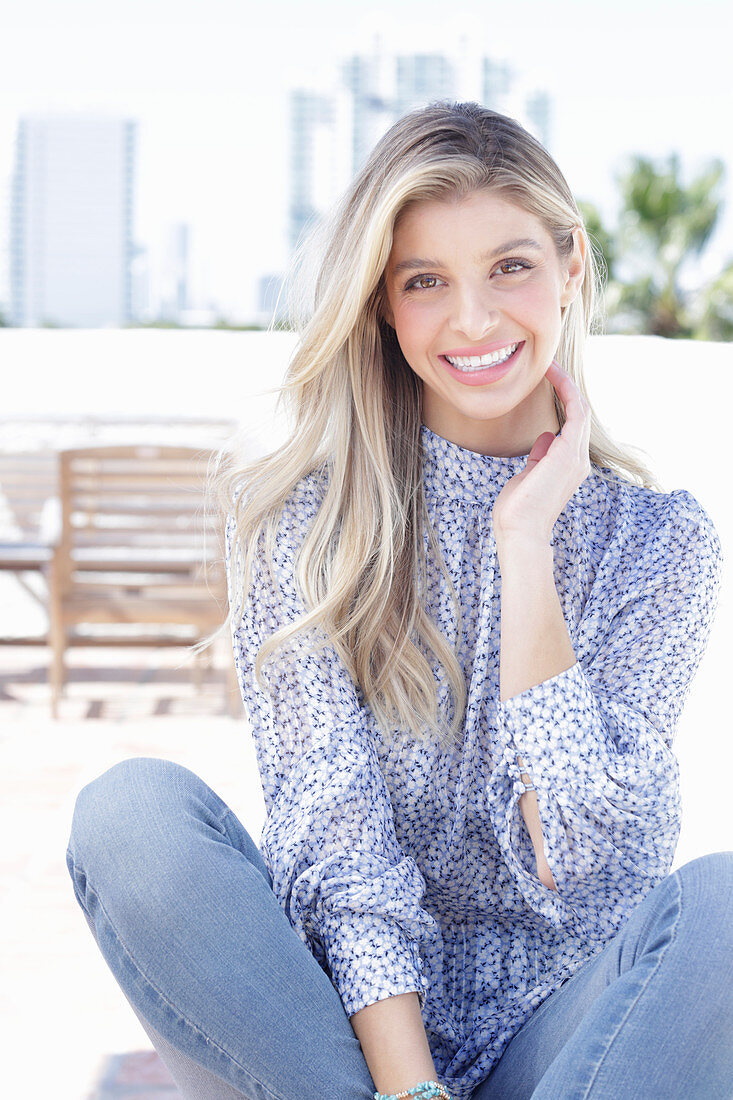 A young blonde woman wearing a blue-and-white patterned top and jeans