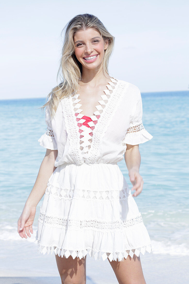 A young blonde woman wearing a white embroidered summer dress