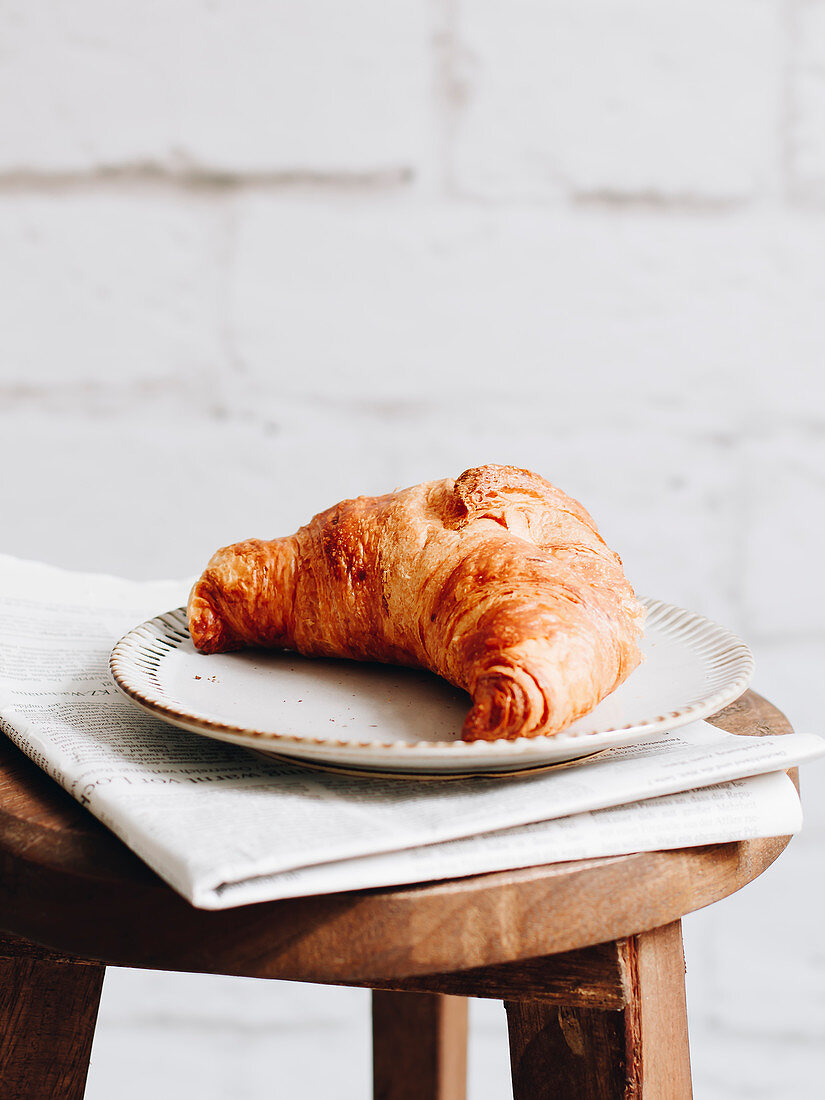 Breakfast croissant and newspaper on a wooden stool