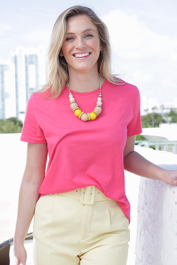 A young blonde woman wearing a pink t-shirt and a pair of light trousers