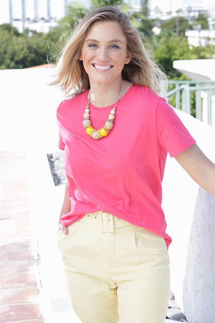 A young blonde woman wearing a pink t-shirt and a pair of light trousers