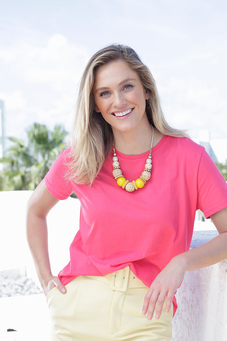 A young blonde woman wearing a pink t-shirt and a pair of light trousers