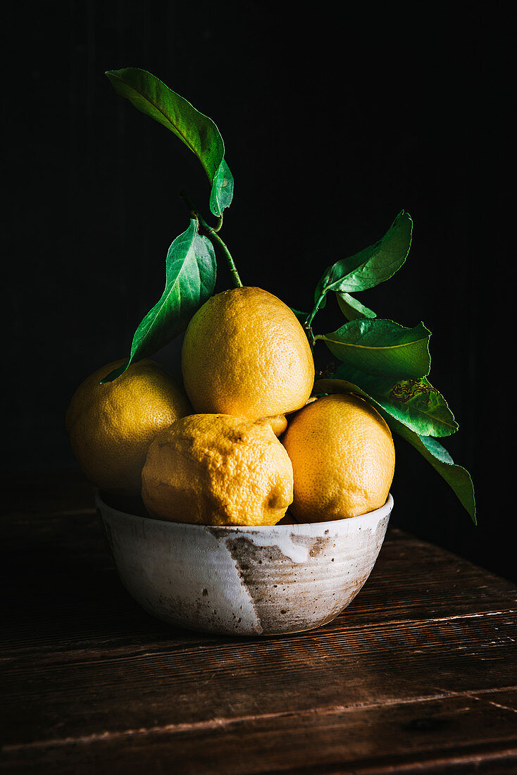 Stillleben mit Zitronen in einer Schüssel vor schwarzem Hintergrund