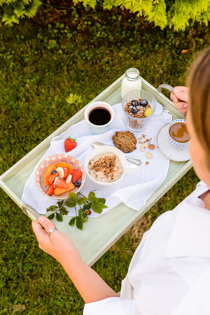 Frau trägt Tablett mit gesunden Frühstücks-Variationen