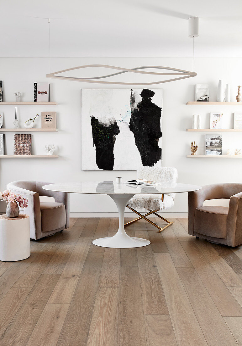 Paintings and picture ledges on wall behind armchairs at designer table