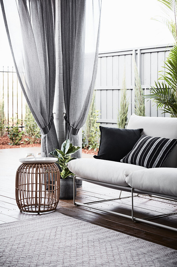 Sofa und Beistelltisch auf überdachter Terrasse mit Gardinen im Garten