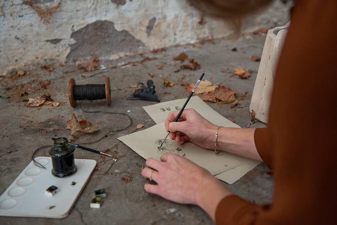 Woman drawing on cards, black paint and autumn leaves on concrete surface