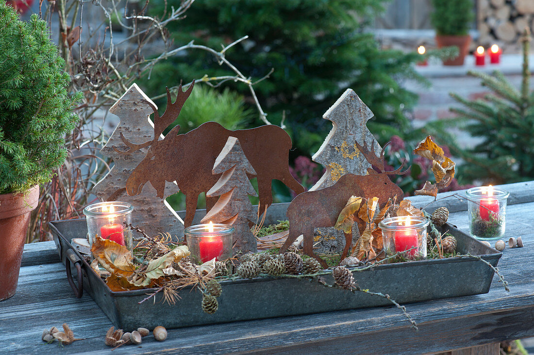 Forest motif on a zinc tray: small wooden fir trees, rust moose silouettes, pinecones, lanterns, leaves, and moss