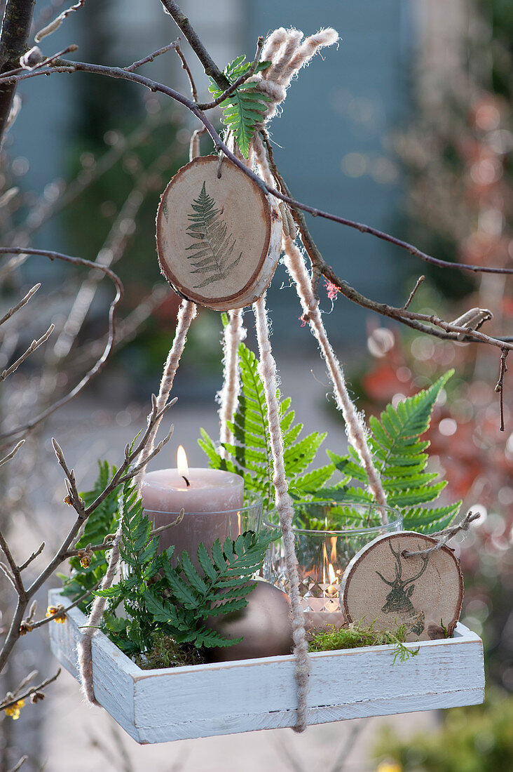 Hanging Christmas decorations with lanterns, fern leaves and homemade pendants made of wooden discs