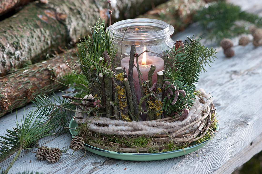 Mason jar as a lantern in a wreath of clematis tendrils, woolen cord and moss, covered with branches