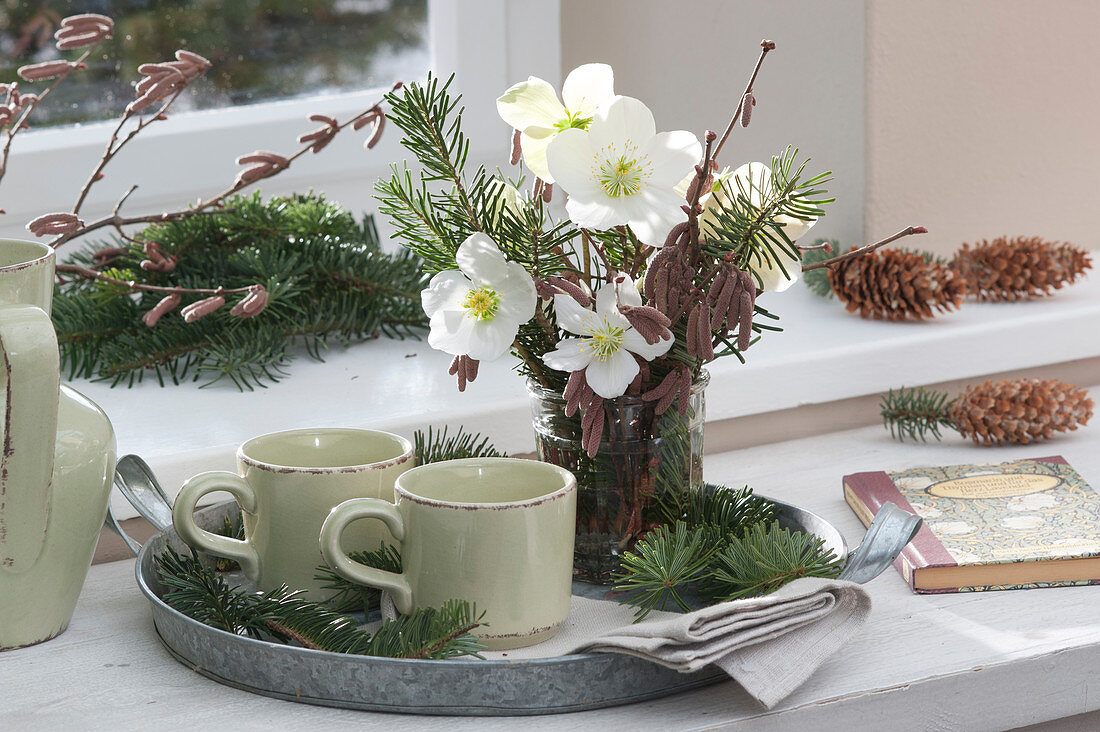 Small Christmas bouquet of Christmas roses, fir branches and hazel branches on a tray with cups