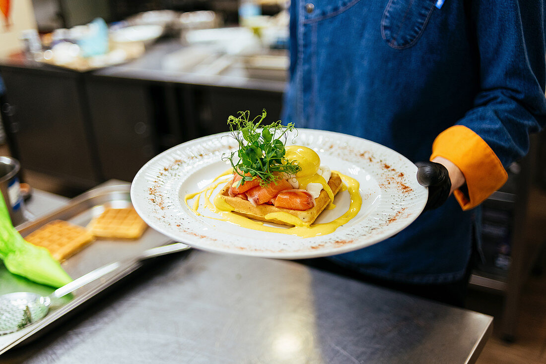 Chefkoch hält Teller Toast mit pochiertem Ei, Lachs und Senfsauce