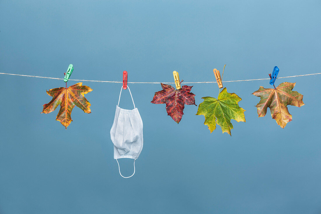 Face mask hanging from clothesline with autumn leaves