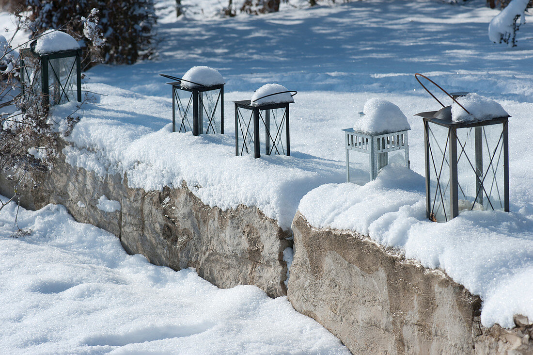 Natural stone wall and lanterns in the snowy garden
