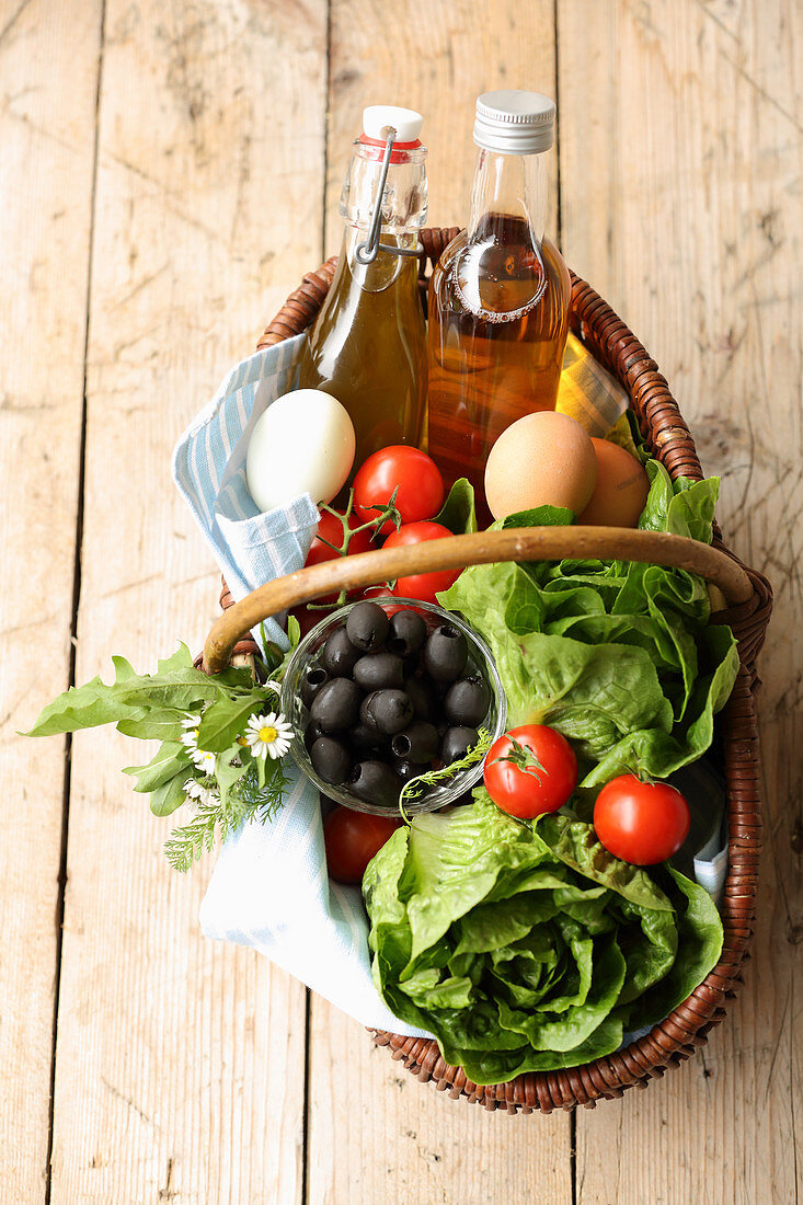 Korb mit Salatköpfen, Tomaten, Eiern, Oliven, Öl und Essig