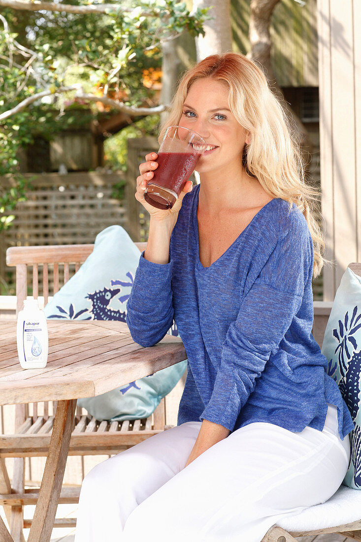 Blonde Frau in blauem Shirt und weißer Hose mit einem Drink