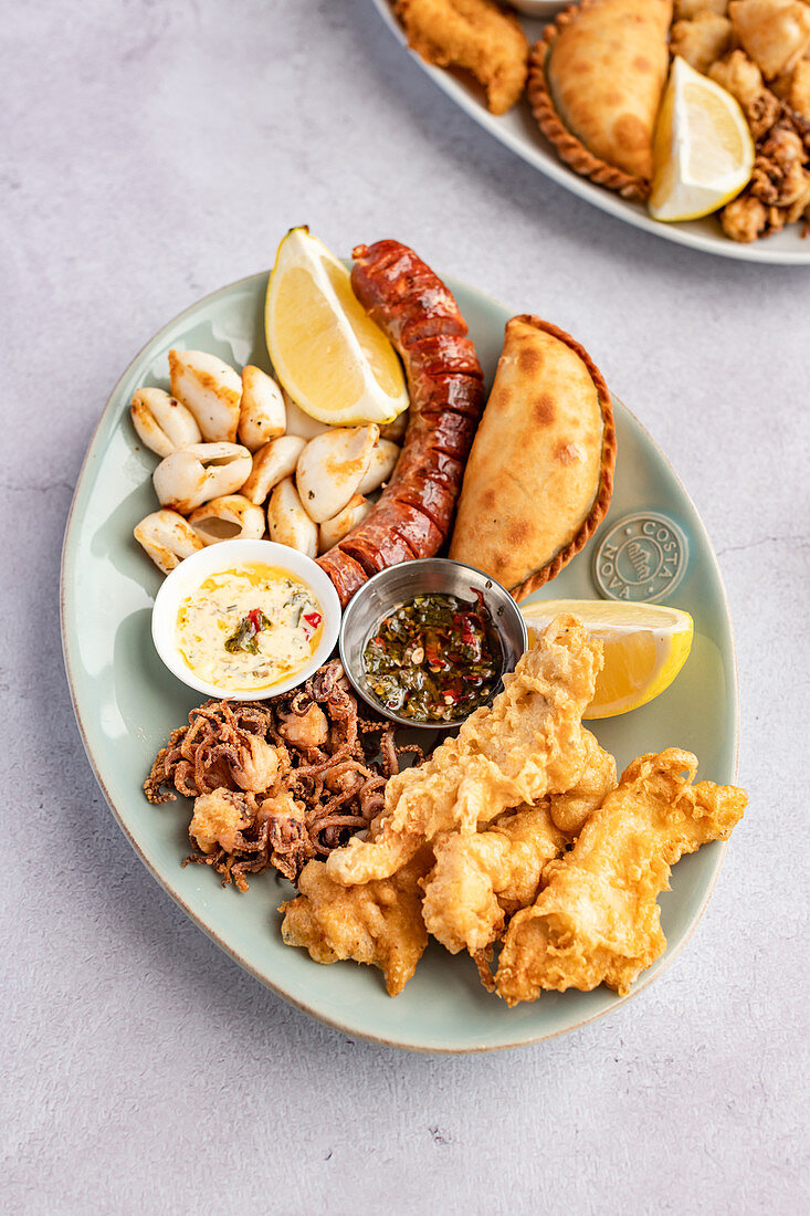 Grillplatte mit Calamari, Fisch, Kolbasa, Empanadas und Dips