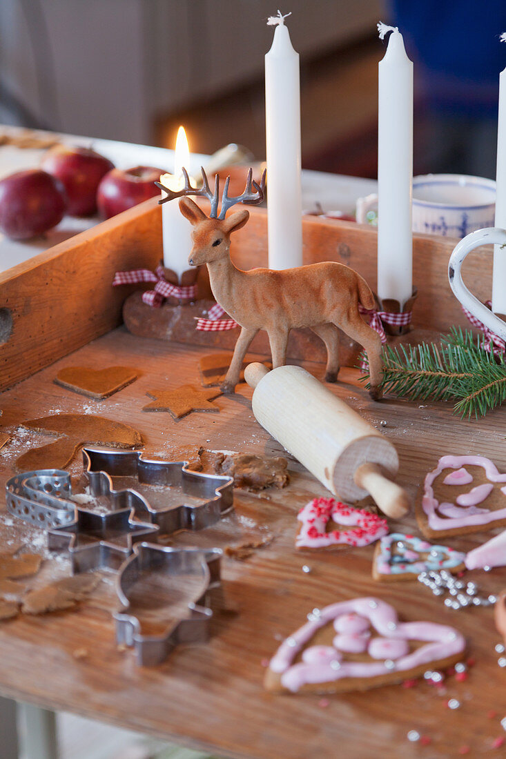 Wooden board with candles, deer figure, rolling pin, gingerbread, and cookie cutters