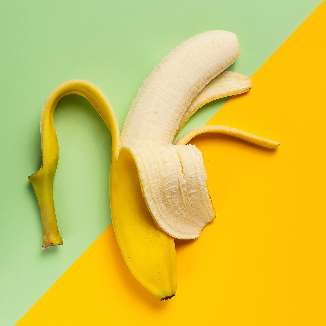 Halb geschälte Banane auf grünem und gelbem Hintergrund