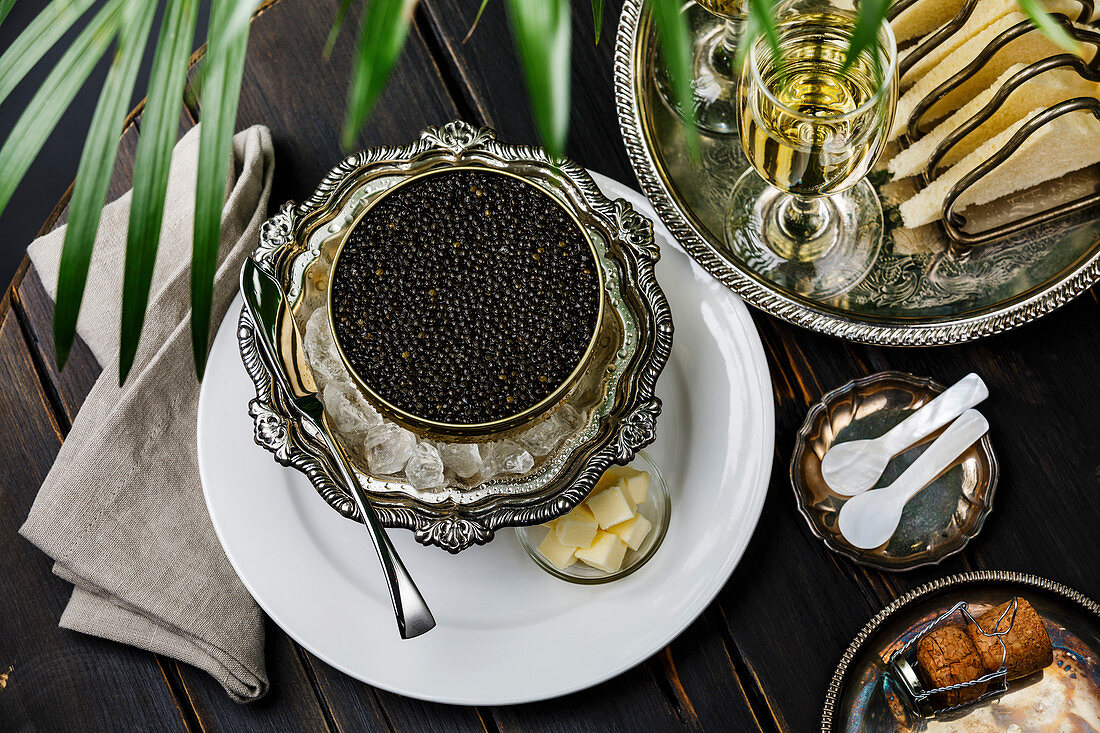 Schwarzer Kaviar in Dose auf Eis in silberner Schüssel serviert mit Champagner