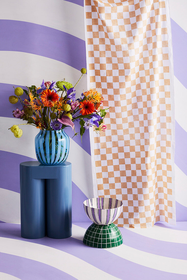 Vase of flowers on stool against purple and white striped wall