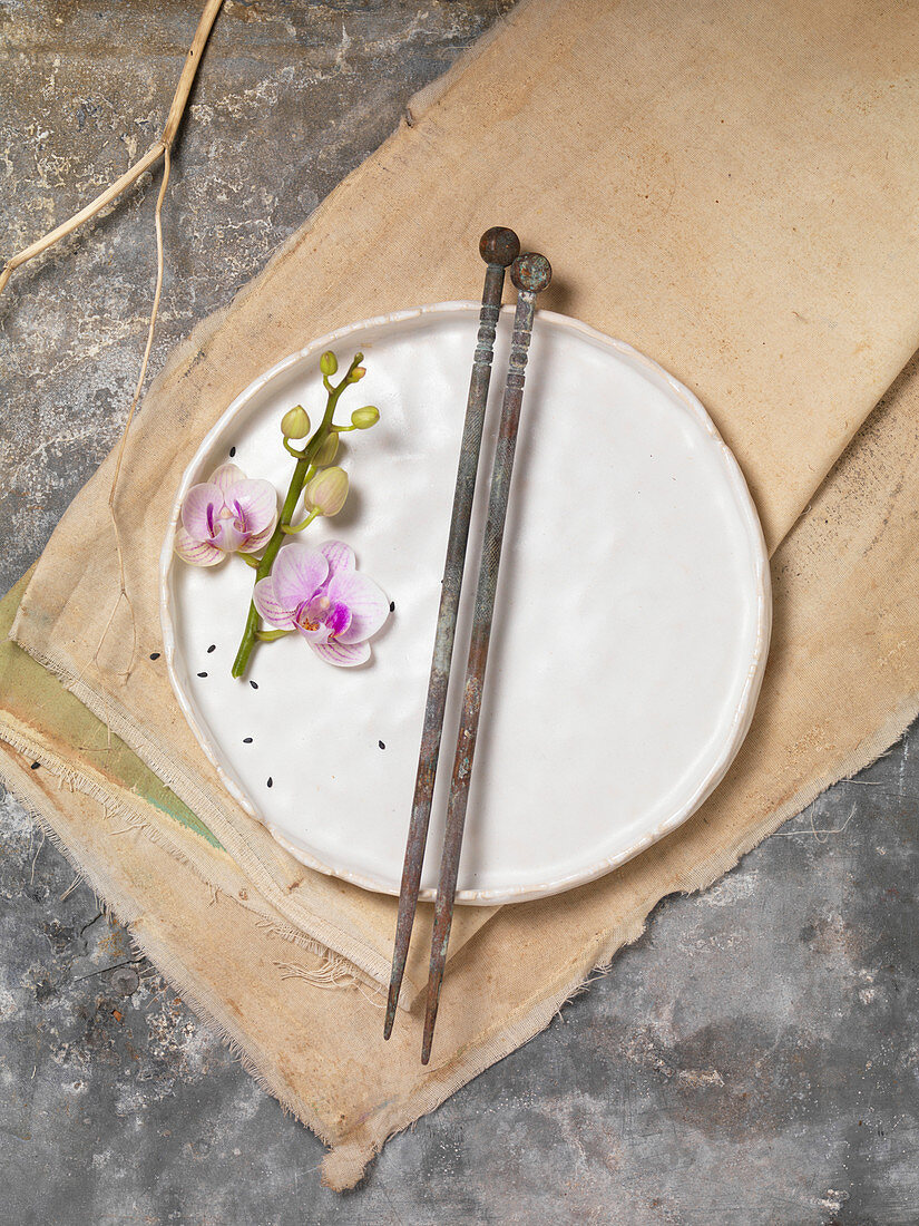 Orchideenblütenzweig und antike Essstäbchen auf weißem Teller und Leinentuch