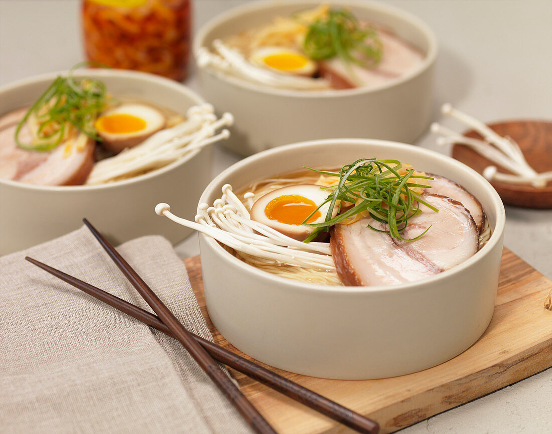 Bowls of Ramen Noodle Soup with Seasoned Egg, Pork, Enoki Mushrooms and Green Onions