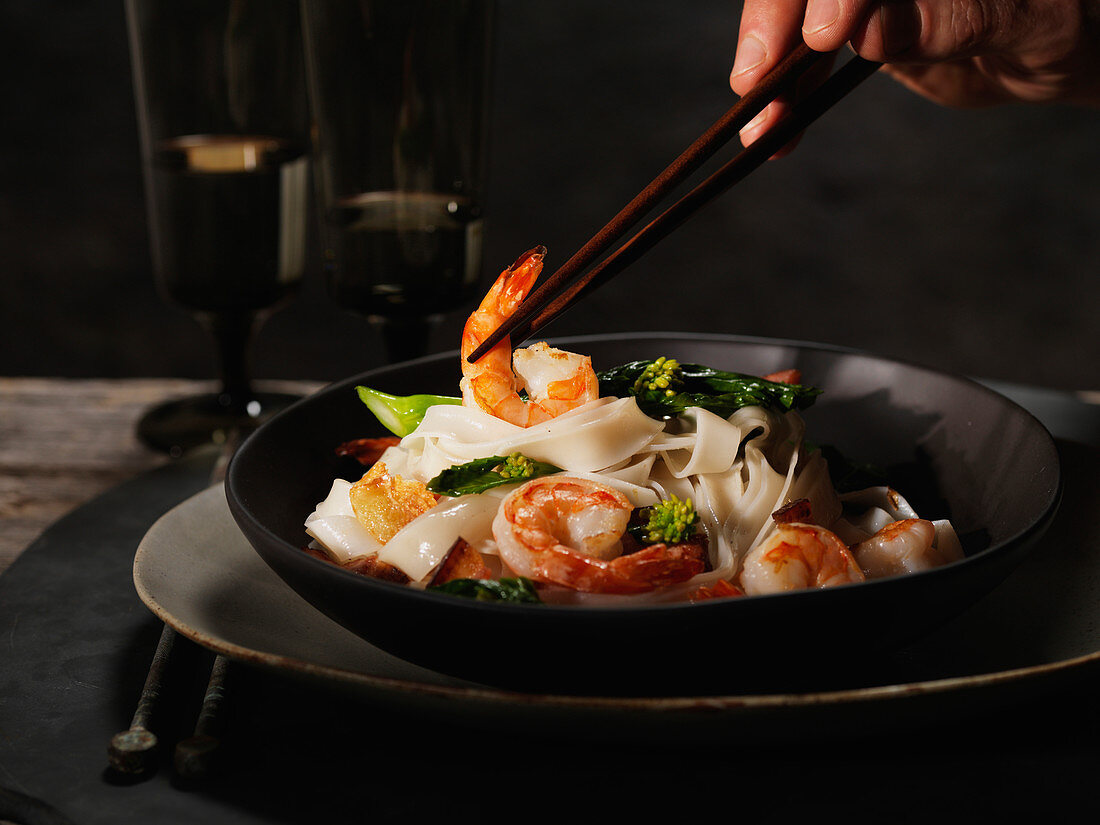 Man’s Hand With Chopsticks Holding Shrimp in Bowl of Noodles