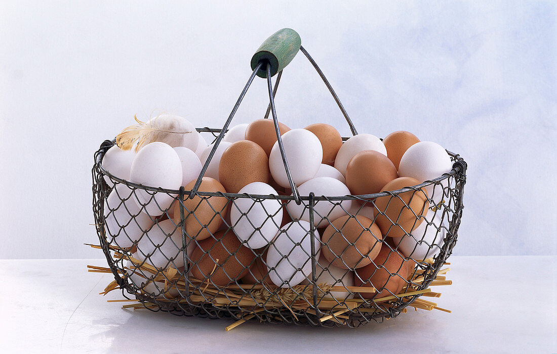 Metal basket with lots of white and brown eggs and straw