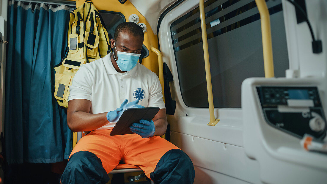 Paramedic in face mask using tablet while in ambulance