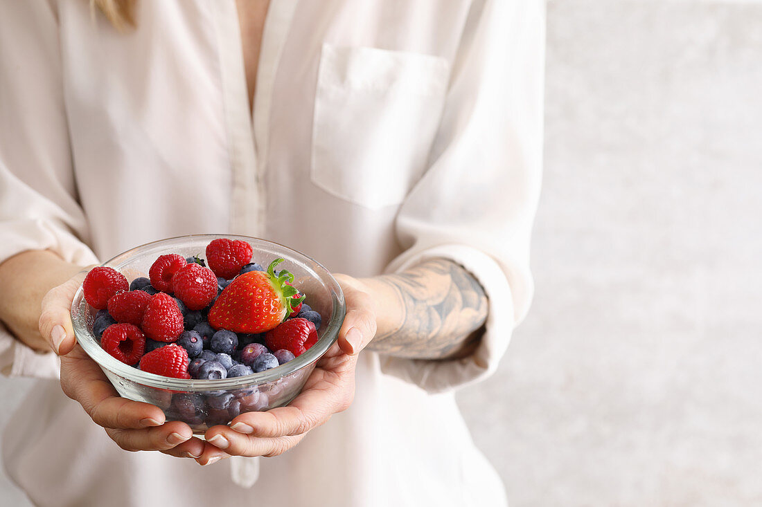 Woman holds a bowl with various fresh berries