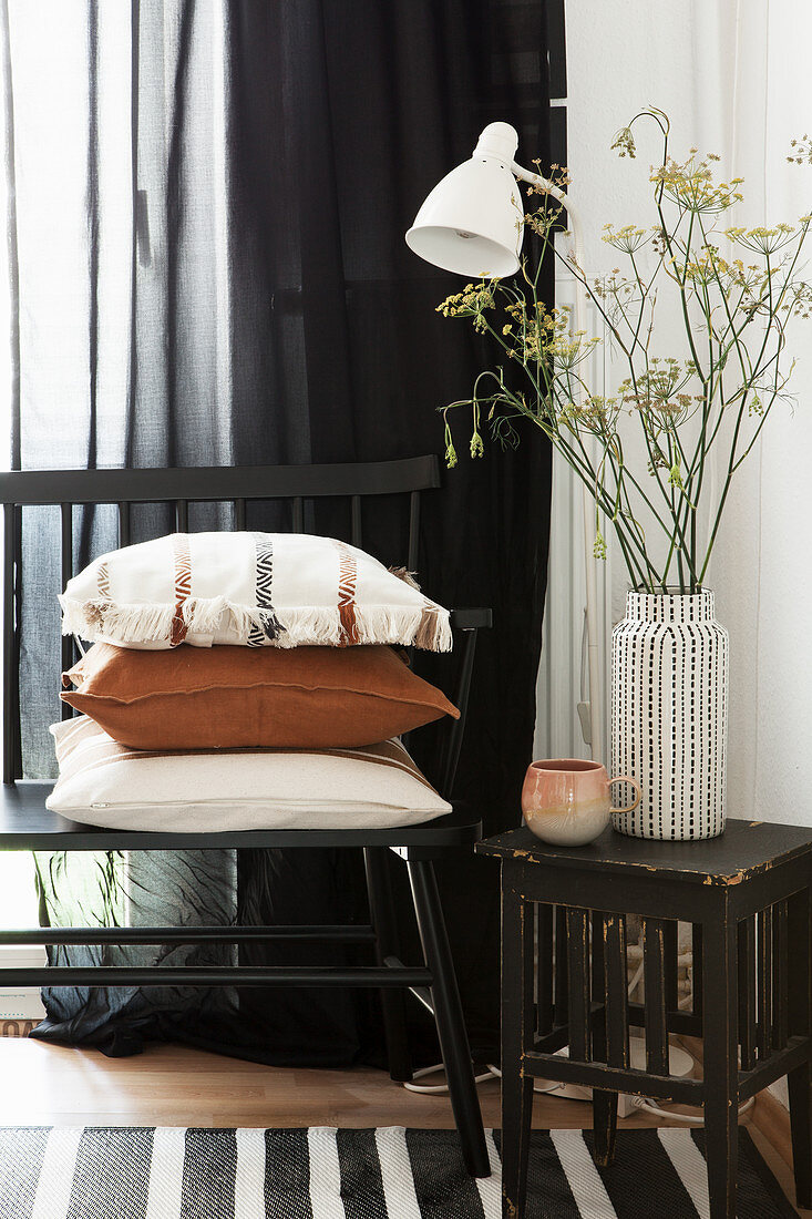 Black bench with cushions and vase of fennel flowers on wooden stool