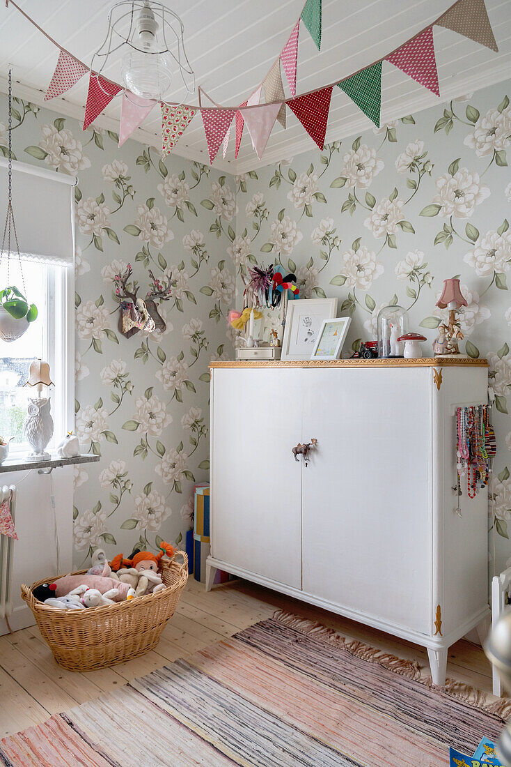 Old cupboard in vintage-style child's bedroom with floral wallpaper